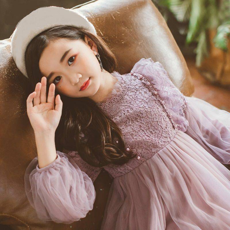 Young girl in a white dress and hat standing in a rustic setting with a plant and table.