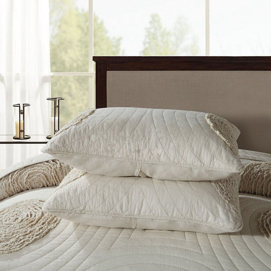 Two white textured pillows on a bed with a wooden headboard and window in the background.