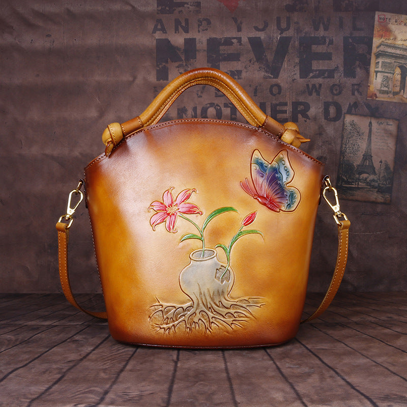 Brown leather handbag with floral and butterfly design on a wooden floor.