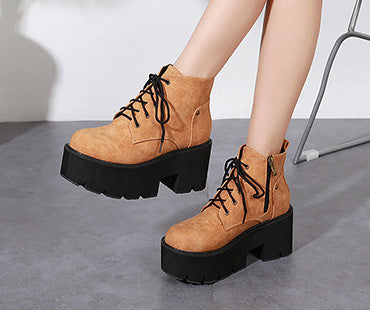 Brown platform boots with black soles worn by a person on a gray surface.