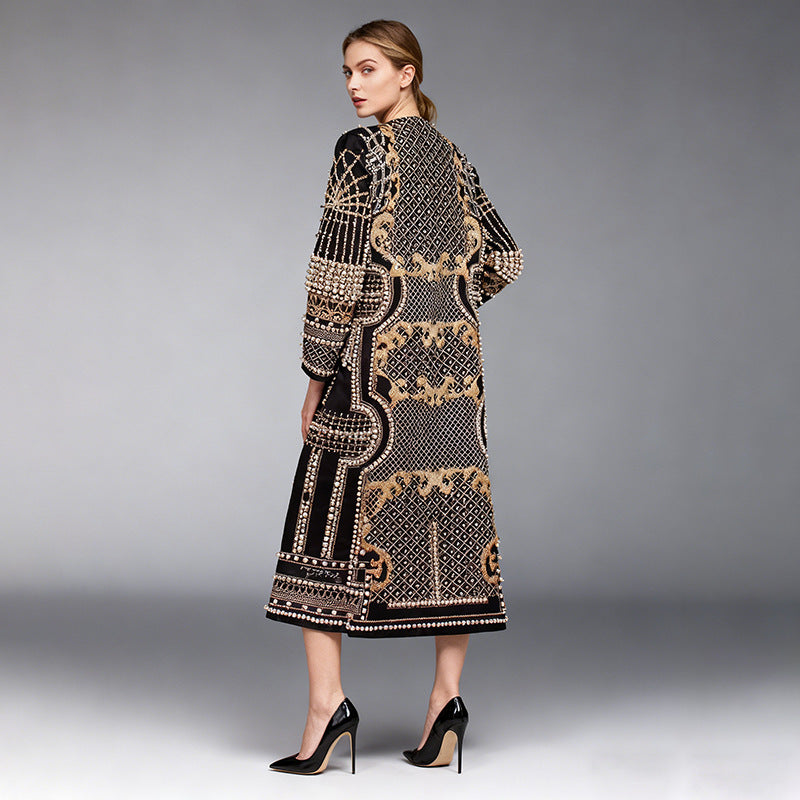 A woman modeling a long black open-front cardigan with intricate gold and beige geometric and floral patterns, shown from a three-quarters back view against a gray studio background.