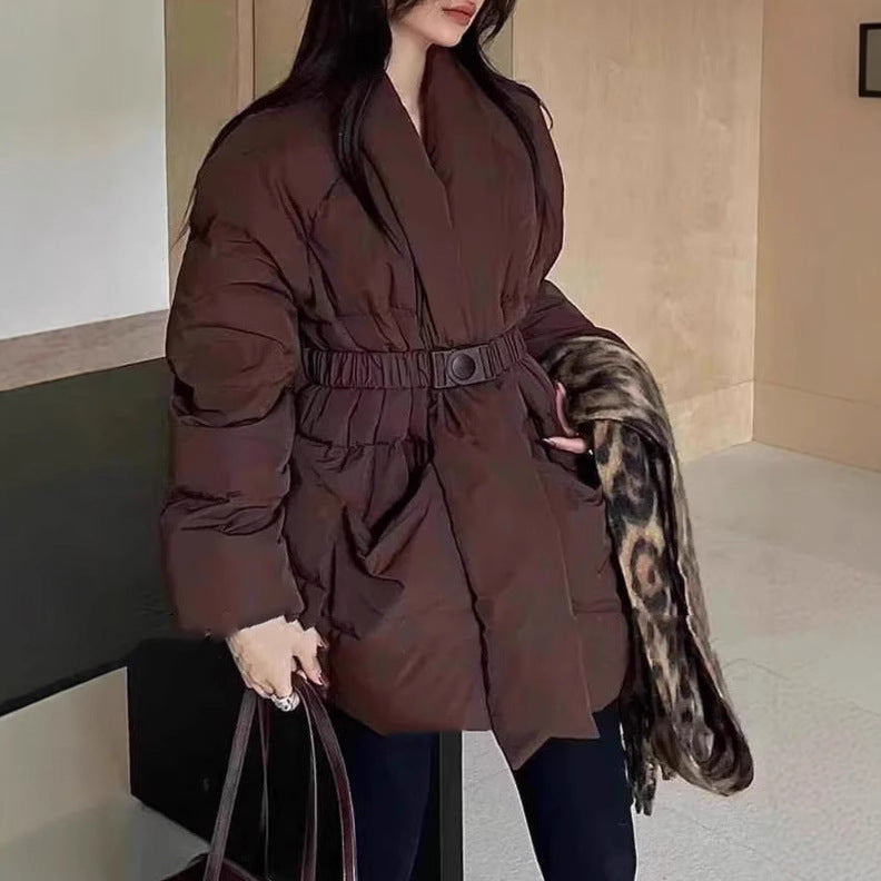 Woman wearing a brown puffer coat holding a patterned scarf indoors.