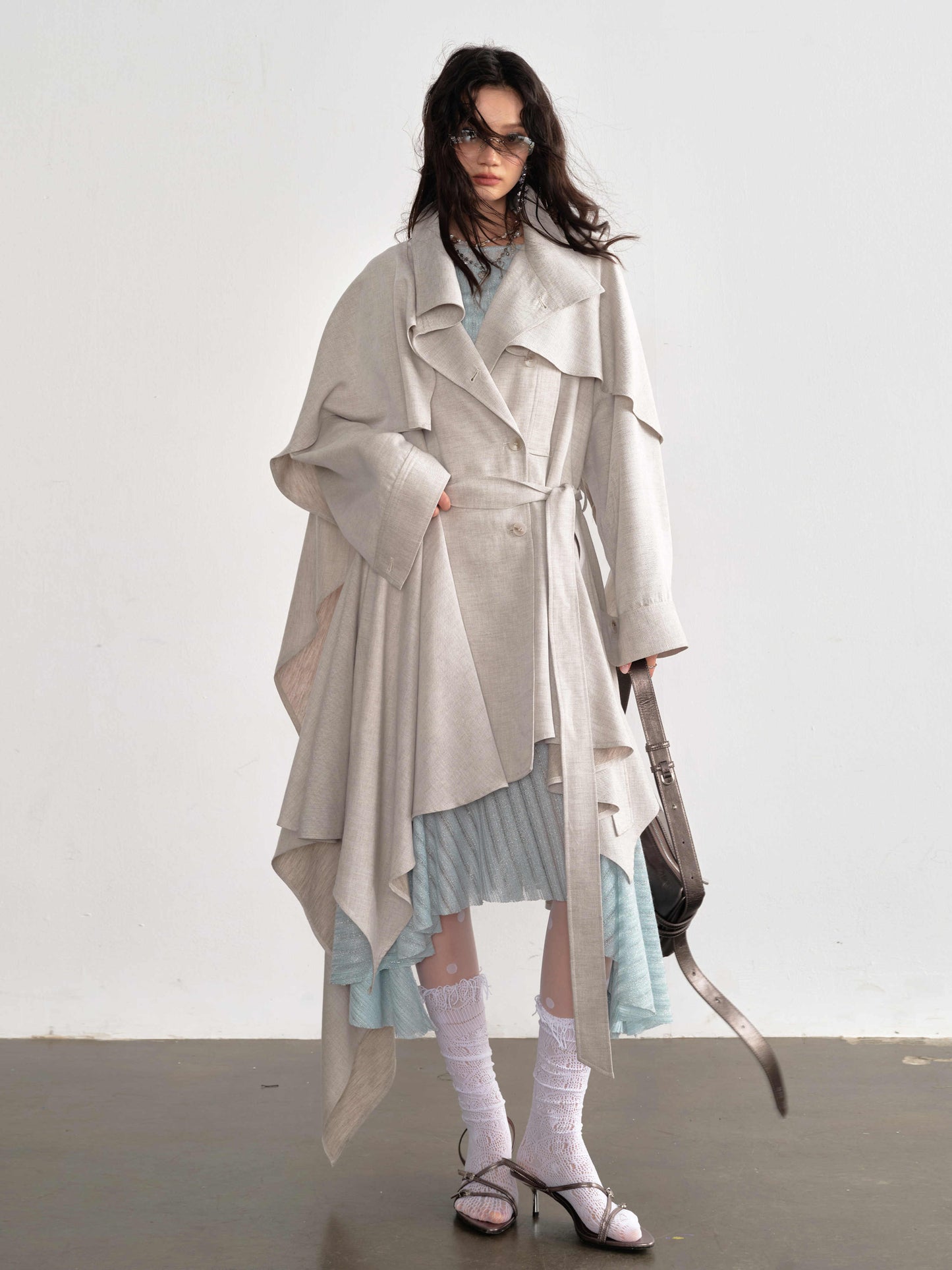 Woman wearing a long, light-colored coat over a dress with a white background
