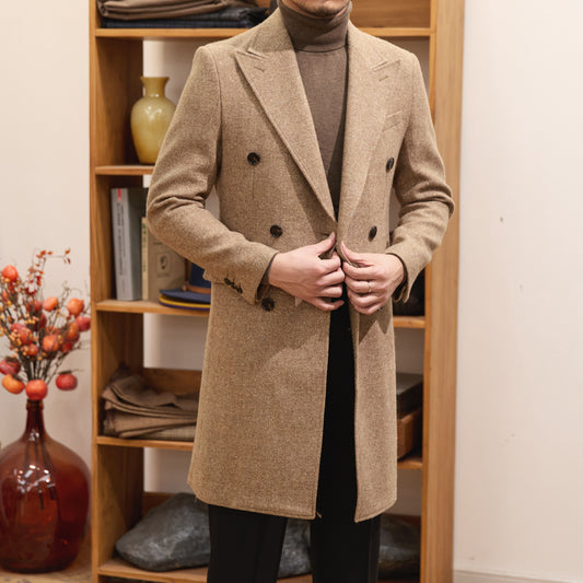 Person wearing a beige overcoat in a room with wooden shelves.