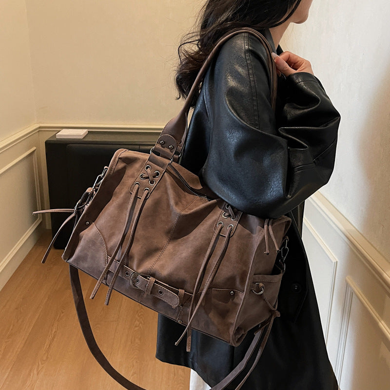 Person wearing a large brown leather bag with a neutral background