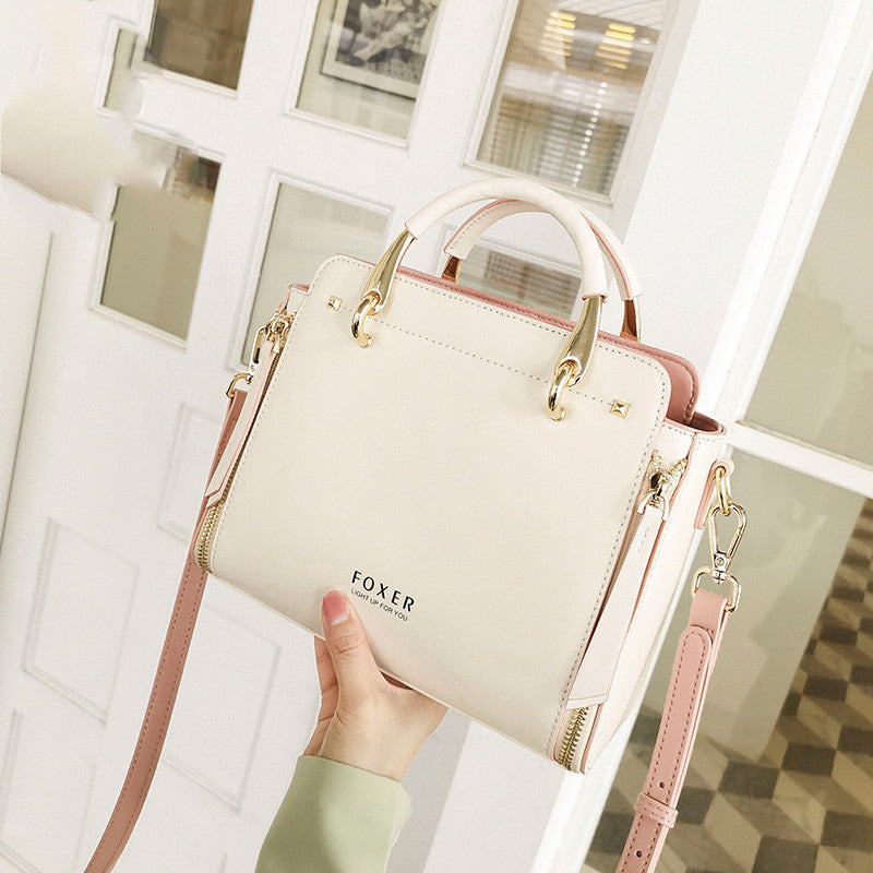 Beige handbag with pink accents held by a hand in front of a window.