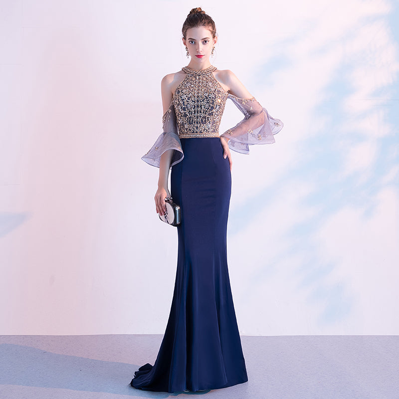 Woman in a formal gown with a blue skirt and embellished top against a light background