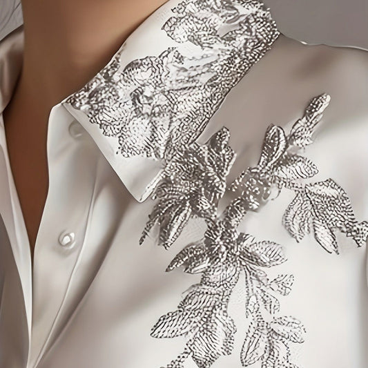 Close-up of a white shirt with silver floral embroidery on a neutral background