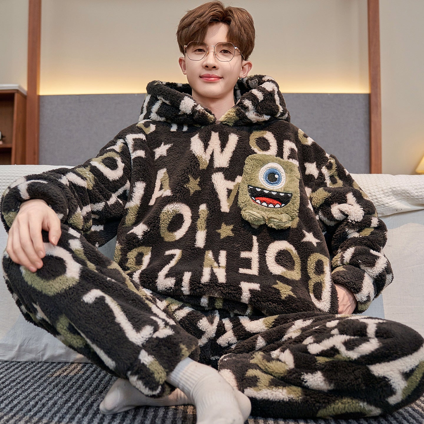 Person wearing a brown fleece onesie with letter patterns and a cartoon character on a couch.