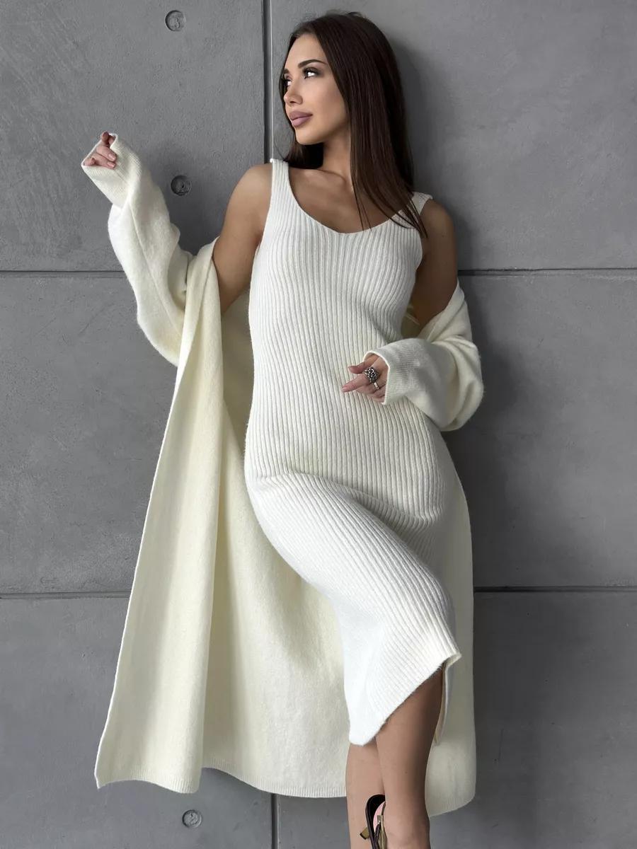 Woman wearing a long white knit dress against a gray wall