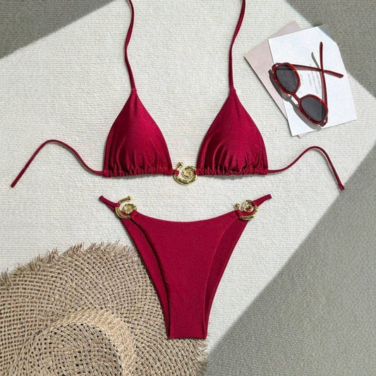 Red bikini set with gold accents on a textured surface with sunglasses and paper.