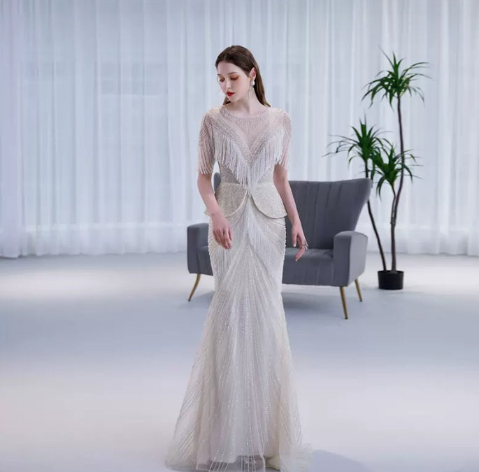Woman in a long, elegant dress standing in a modern room with a gray chair and plant.