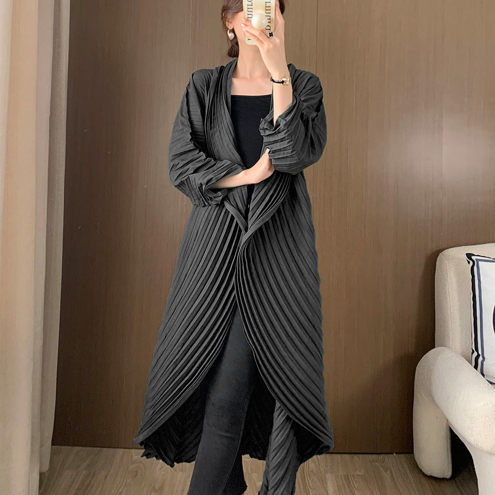 Person wearing a long, dark gray pleated dress against a brown wall.