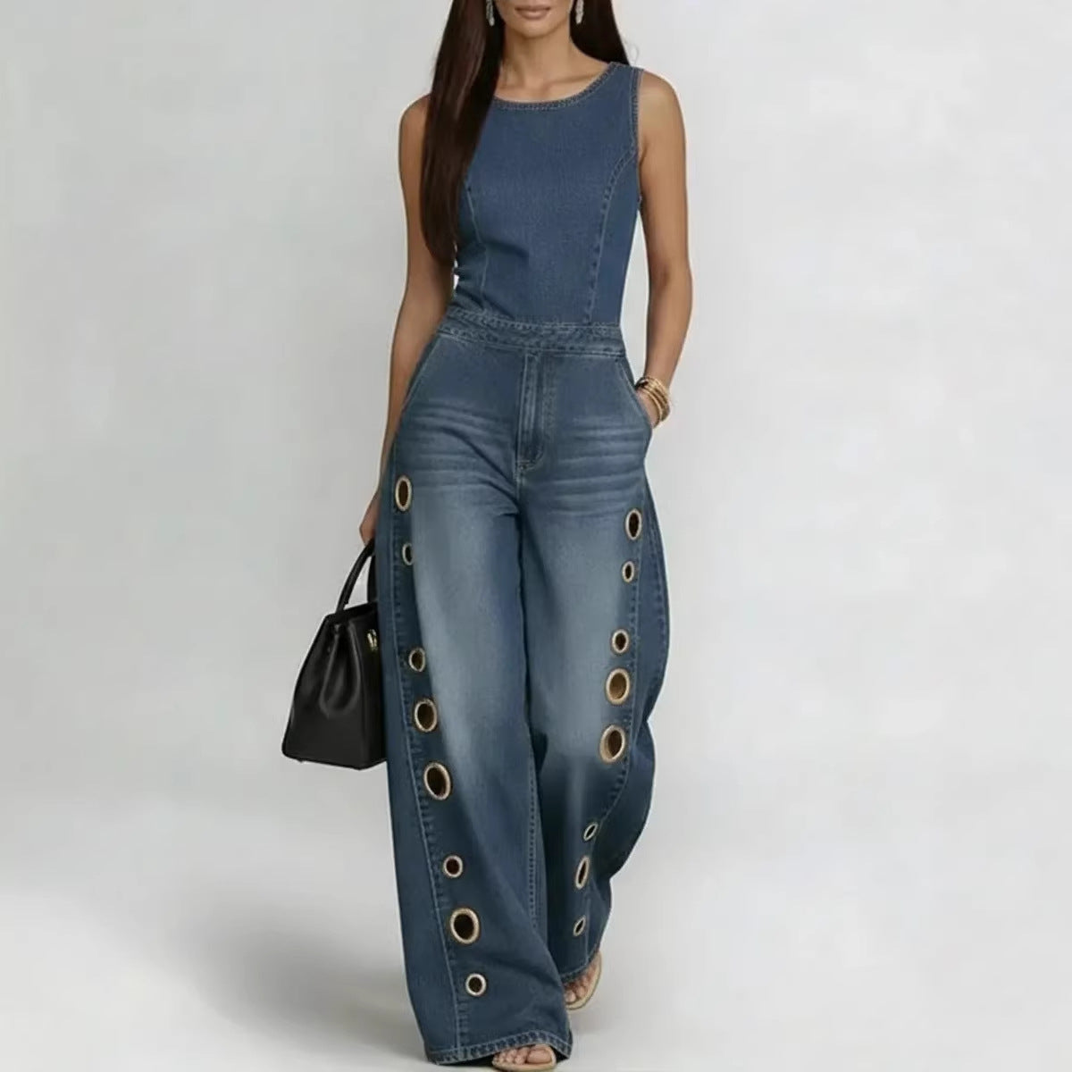 Woman wearing a blue denim jumpsuit with grommet details on a white background
