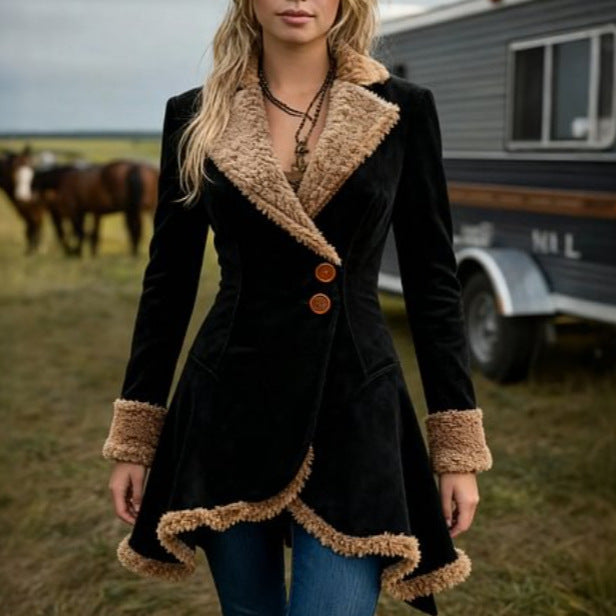 Woman wearing a black coat with brown fur trim standing in a field with horses and a trailer in the background.