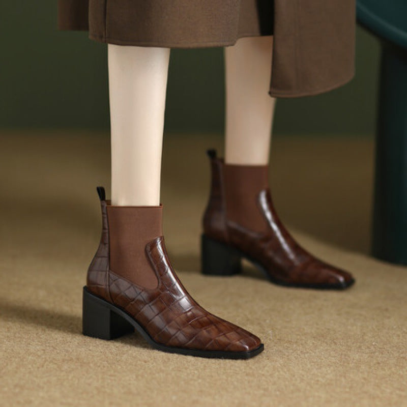 Brown crocodile-patterned boots worn with a brown coat on a blurred background