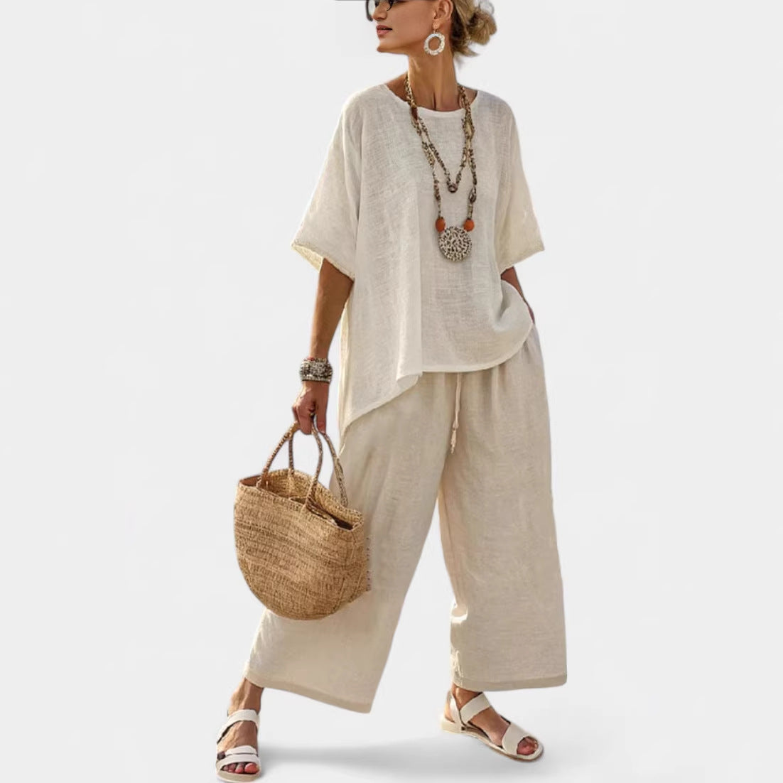 Woman wearing a light-colored outfit with wide-leg pants and a straw bag on a white background