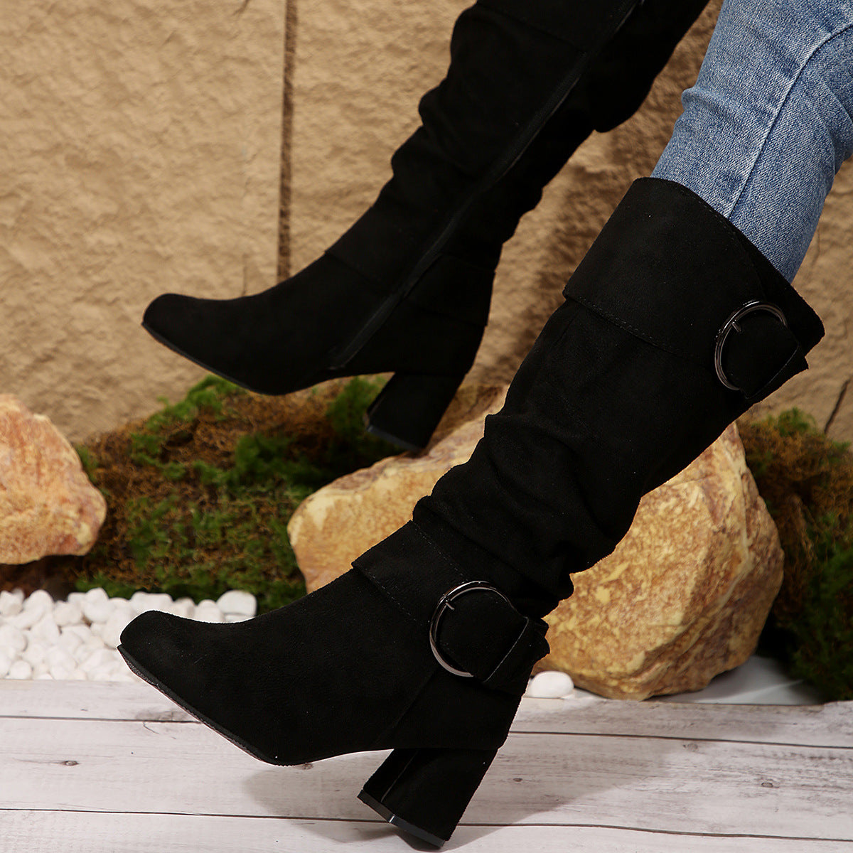 Black knee-high boots with buckles worn by a person on a natural stone background