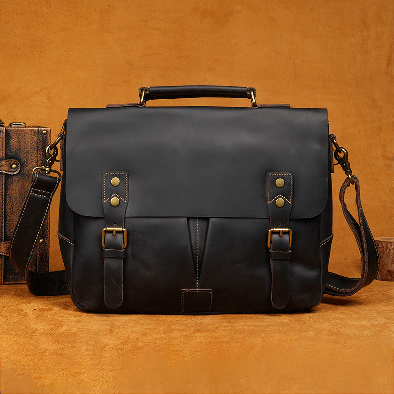 Black leather satchel bag with gold buckles on a brown background