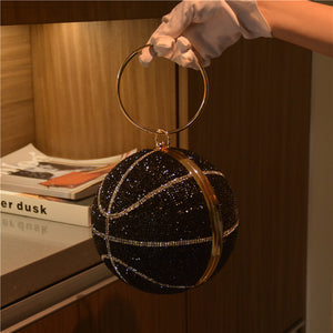Black glittery handbag with gold accents held by a gloved hand against a blurred indoor background.