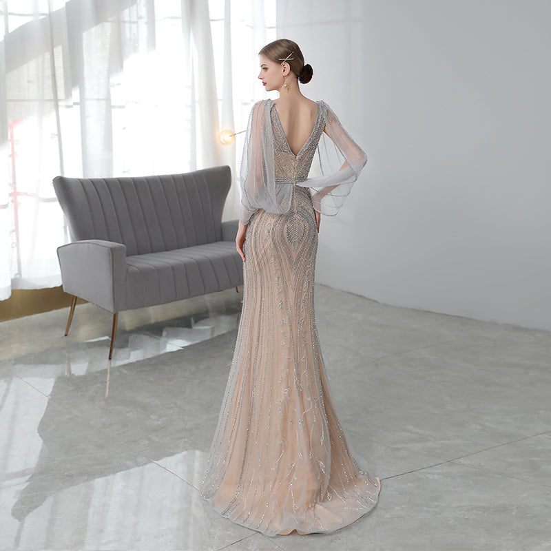 Woman in a elegant dress standing in a modern room with a gray sofa and white walls.