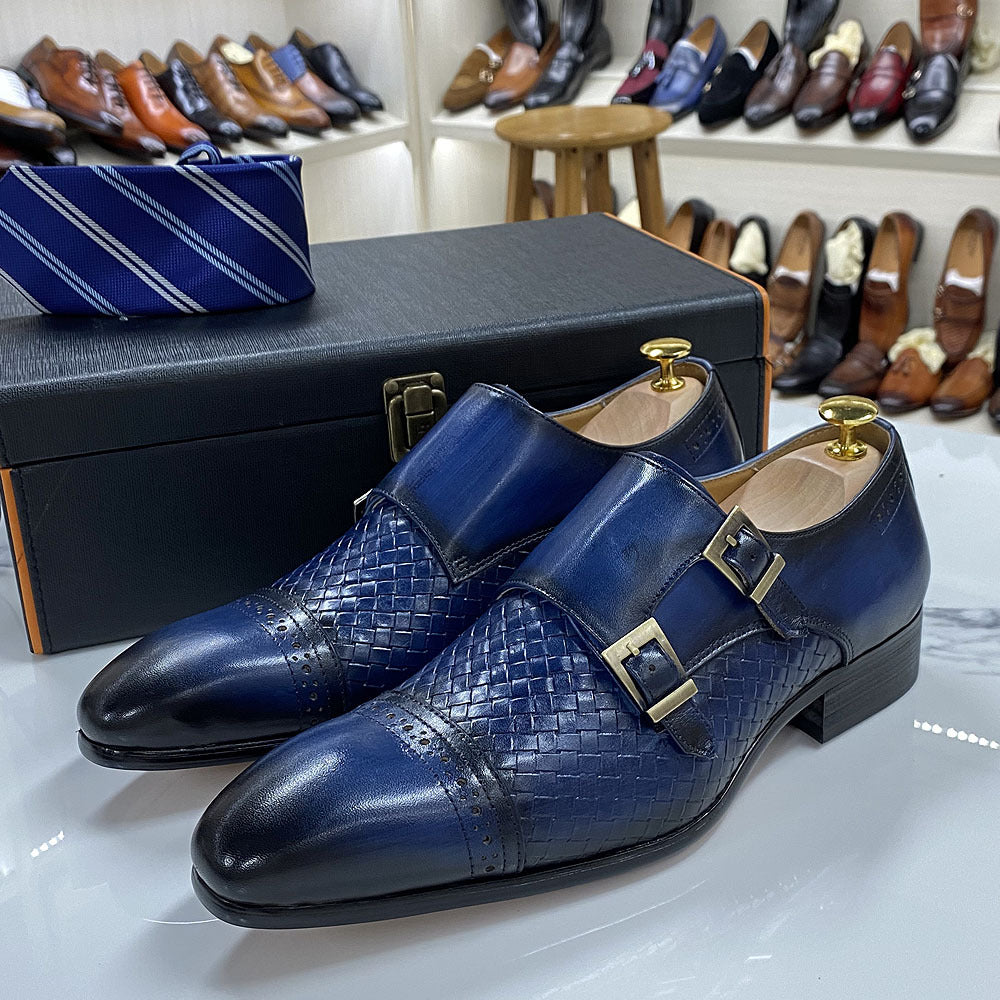 Blue woven dress shoes with gold buckles on a white surface, with a black shoebox and striped tie in the background.