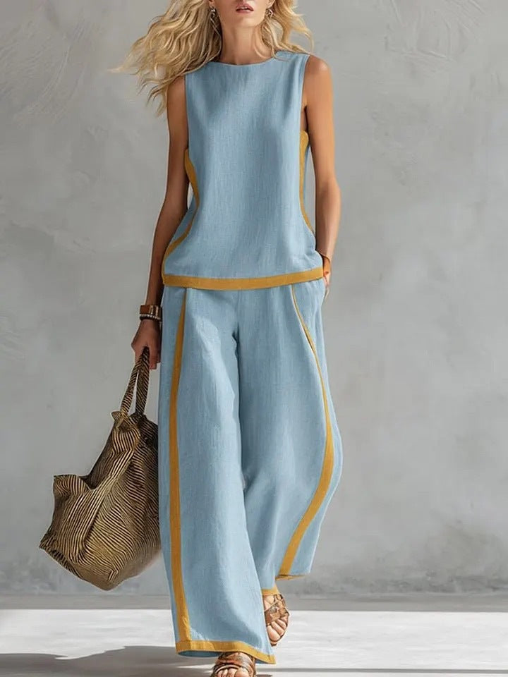 Woman wearing a light blue outfit with yellow accents, holding a woven bag against a gray background.