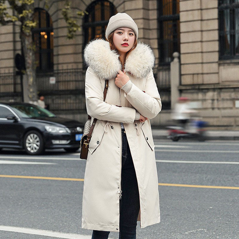 Woman wearing a long beige coat with fur hood on a city street.