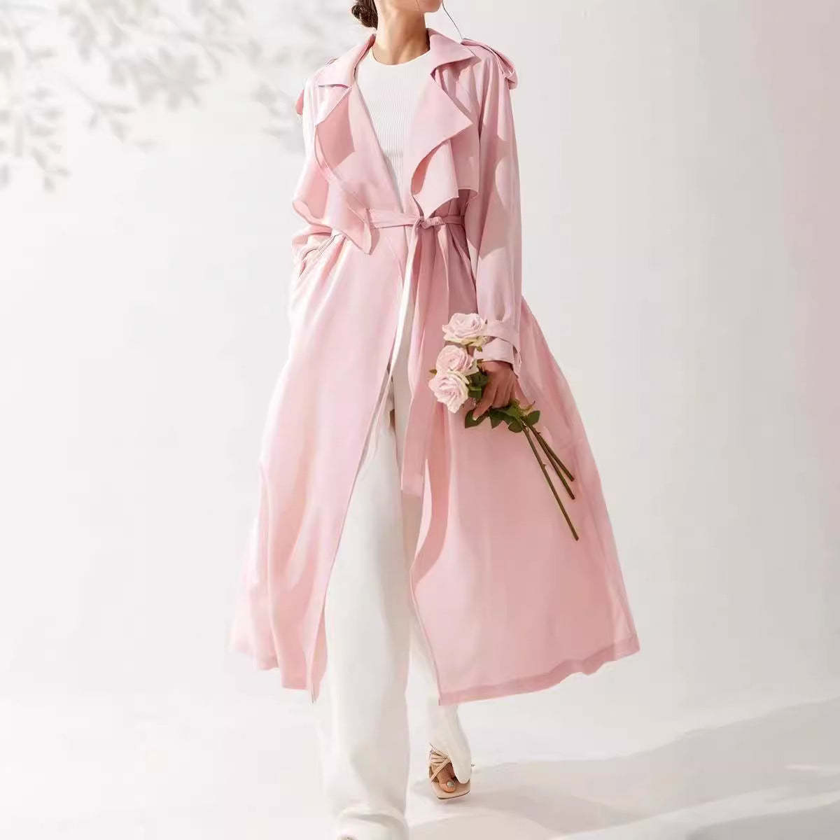 Person wearing a pink trench coat holding flowers on a white background