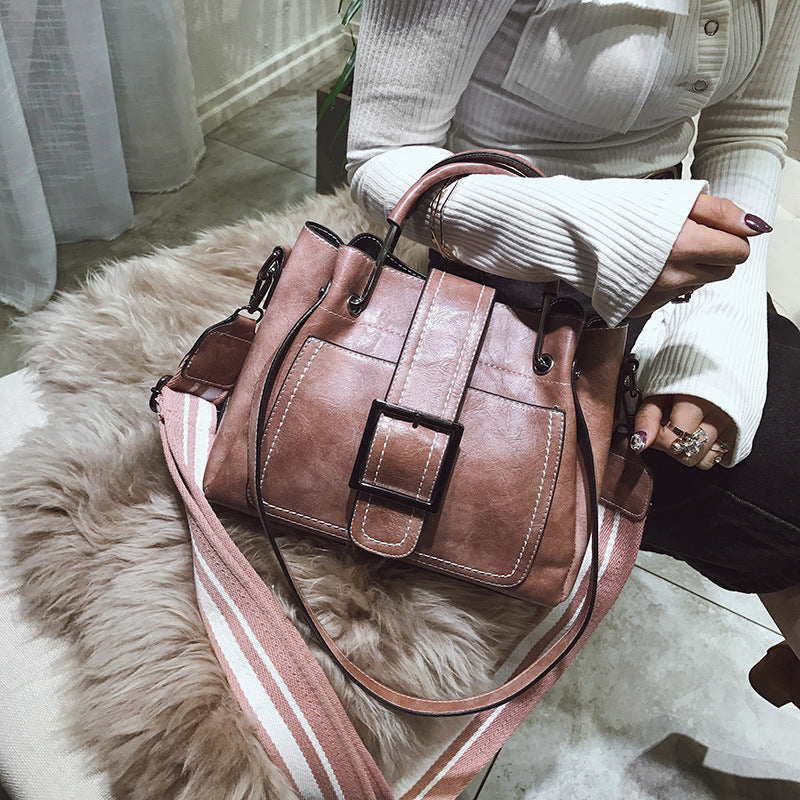 Brown leather handbag with a strap held by a person on a fluffy white rug.