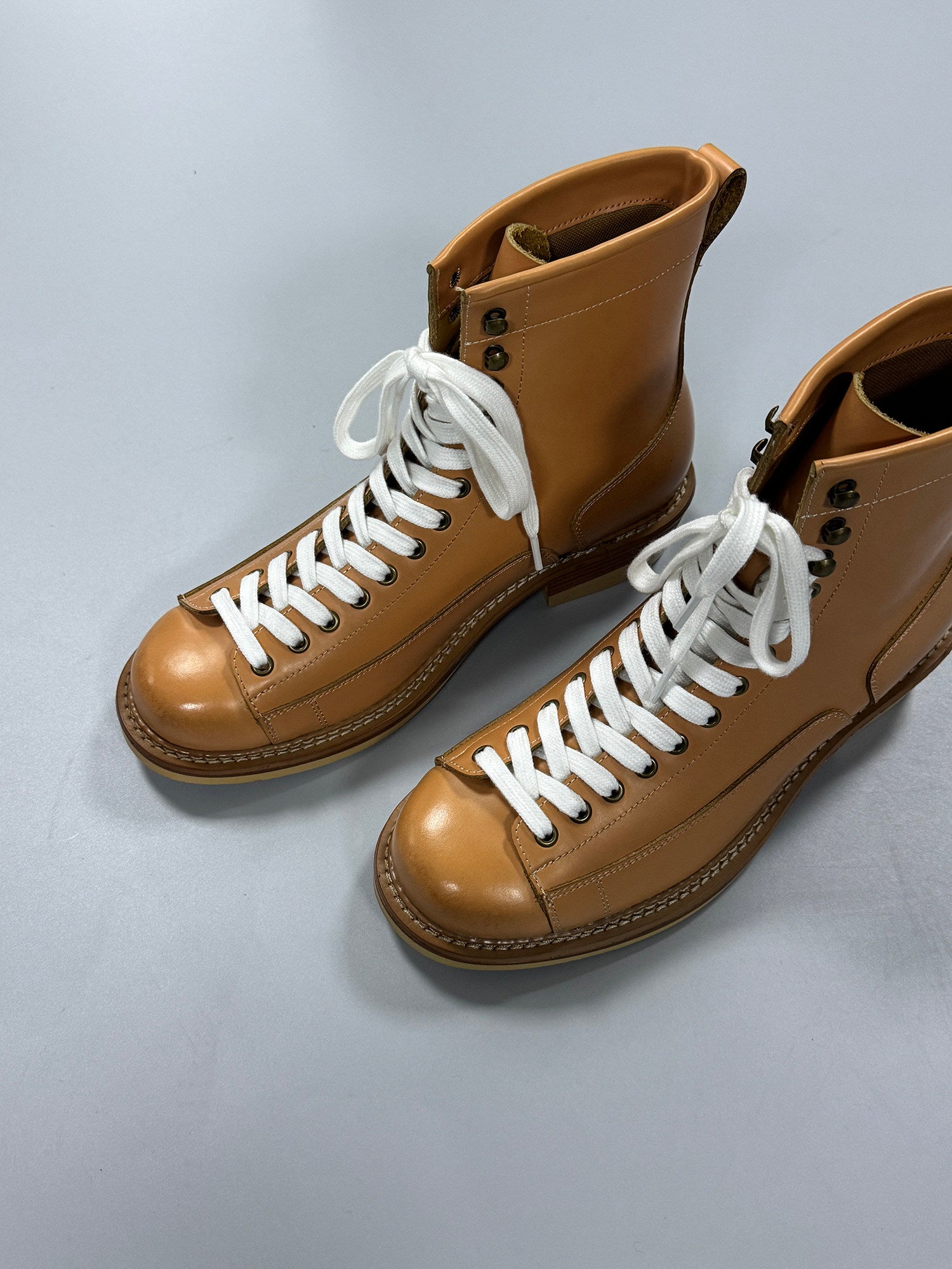 Pair of brown leather boots with white laces on a light gray background