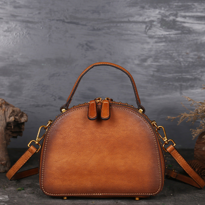 Brown leather handbag with gold accents on a dark textured background