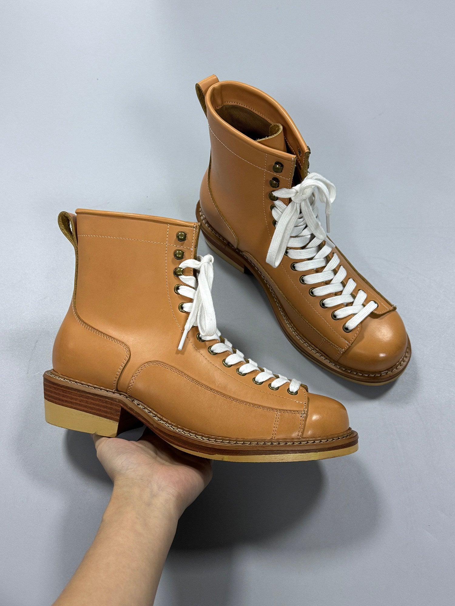 Tan leather boots with white laces held against a light gray background