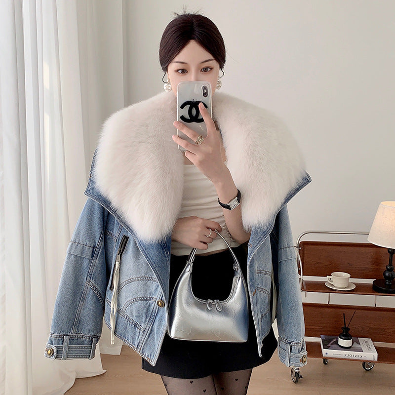 Woman taking a mirror selfie wearing a denim jacket with a fur collar, holding a silver handbag.