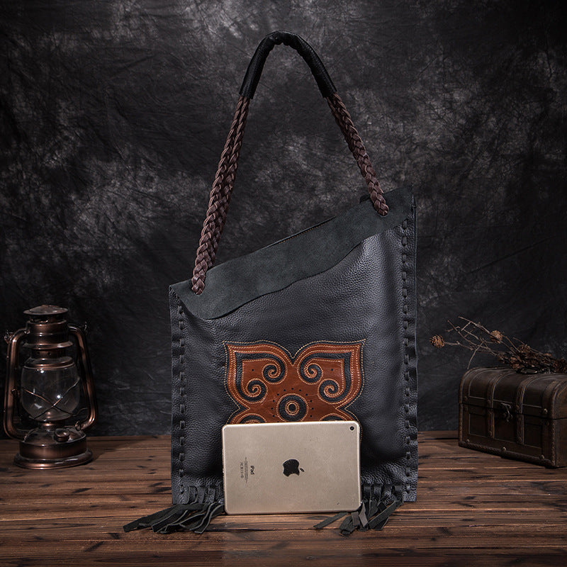 Black leather bag with brown decorative pattern on a wooden surface with a dark background