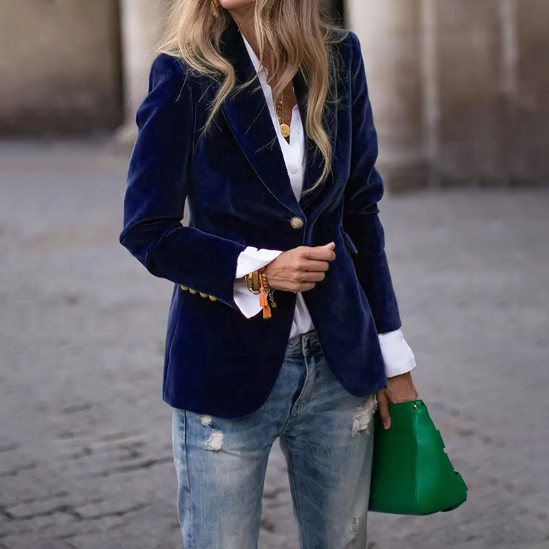 Person wearing a navy blazer, white shirt, and jeans, holding a green handbag.