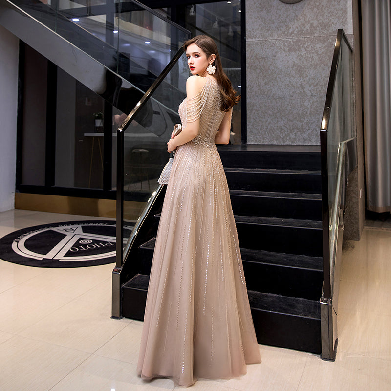 Woman in a beige evening gown standing on a staircase in an elegant interior setting.
