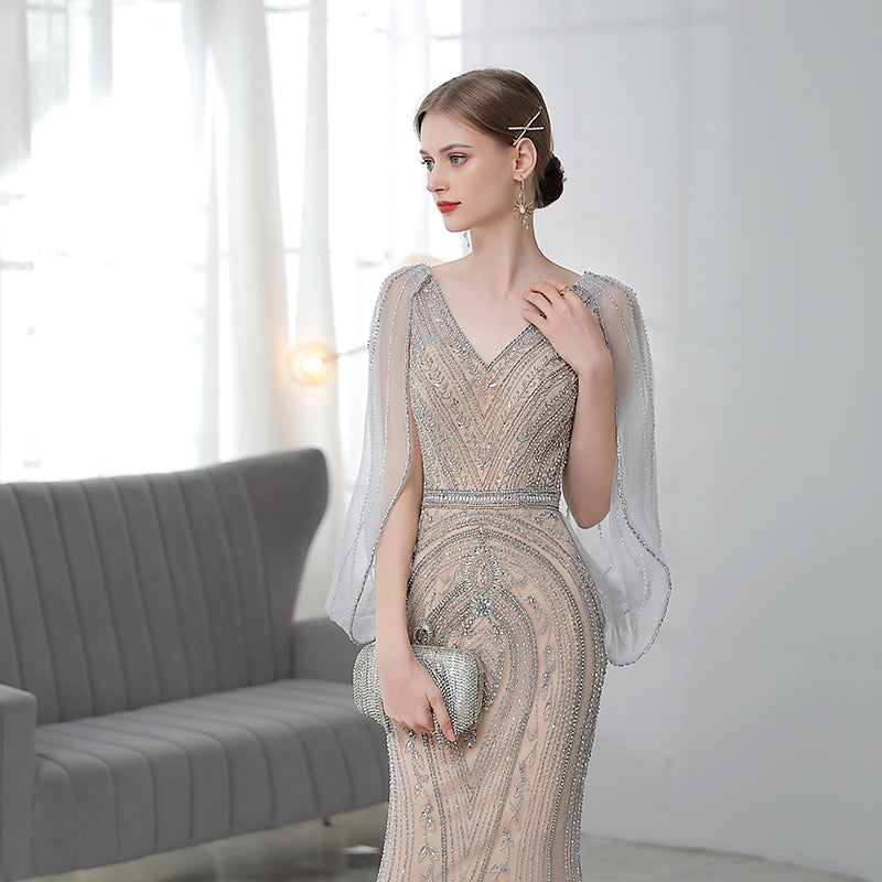 Woman in a elegant dress with sheer sleeves in a room with a gray couch.