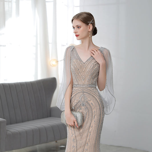 Woman in a elegant dress with sheer sleeves in a room with a gray couch.
