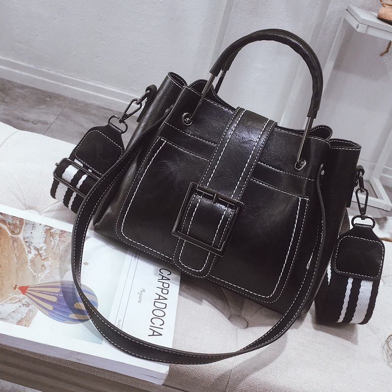 Black handbag with a strap on a surface with a magazine underneath