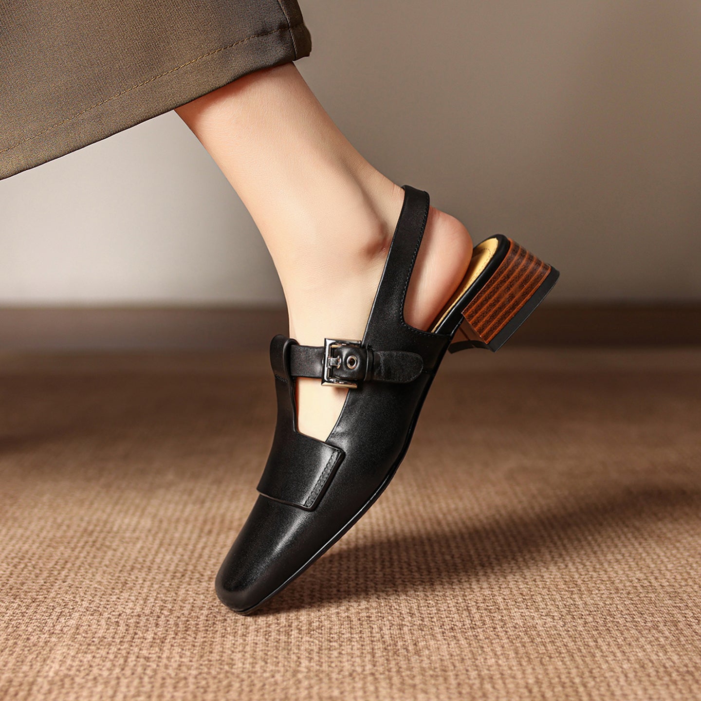 Black sandal with a brown sole worn by a person on a textured surface