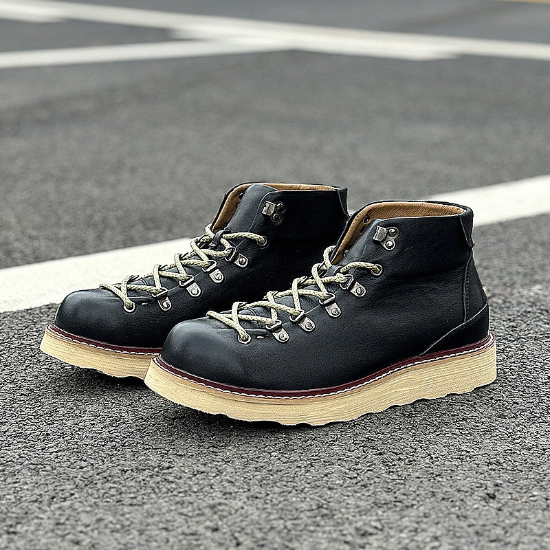 Pair of black leather boots with beige soles on a road surface