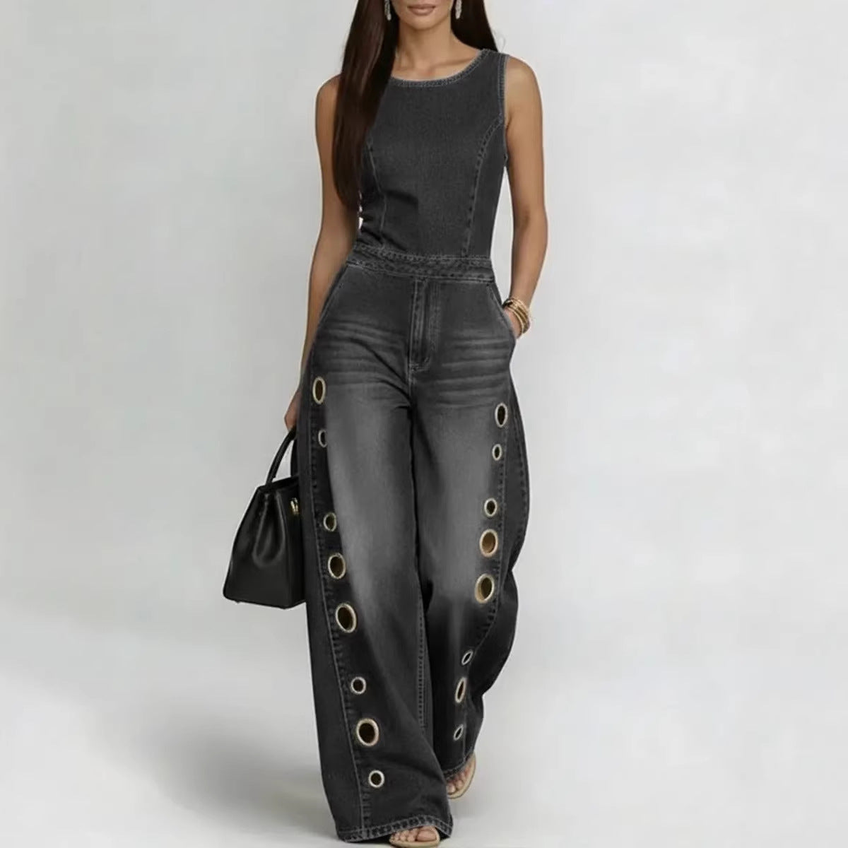 Woman wearing a black denim jumpsuit with grommet details on a white background