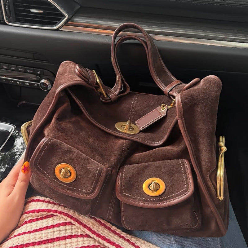 Brown suede handbag with gold accents held by a person inside a car.