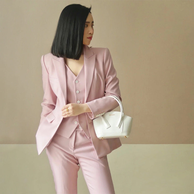 Woman in a pink suit holding a white handbag against a beige background