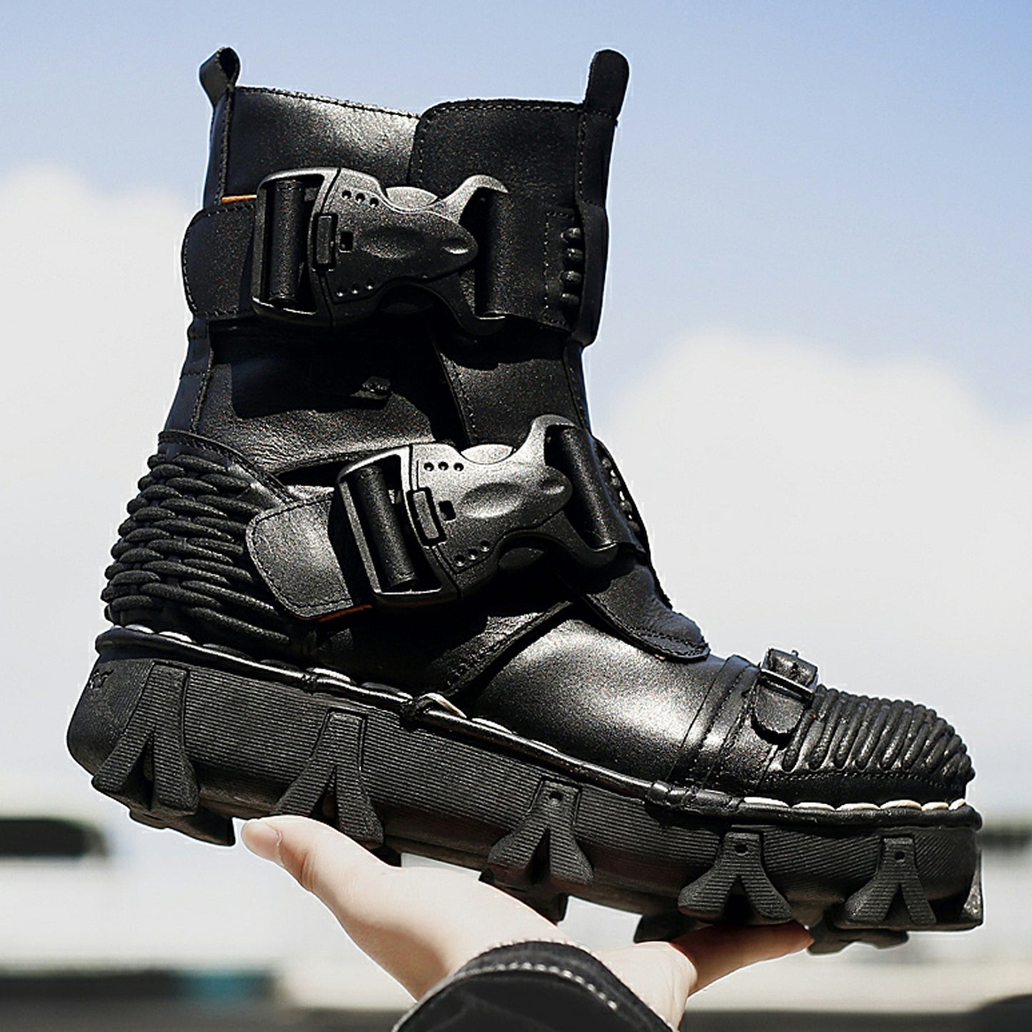 Black high-tech boot with multiple straps held by a hand against a blurred outdoor background