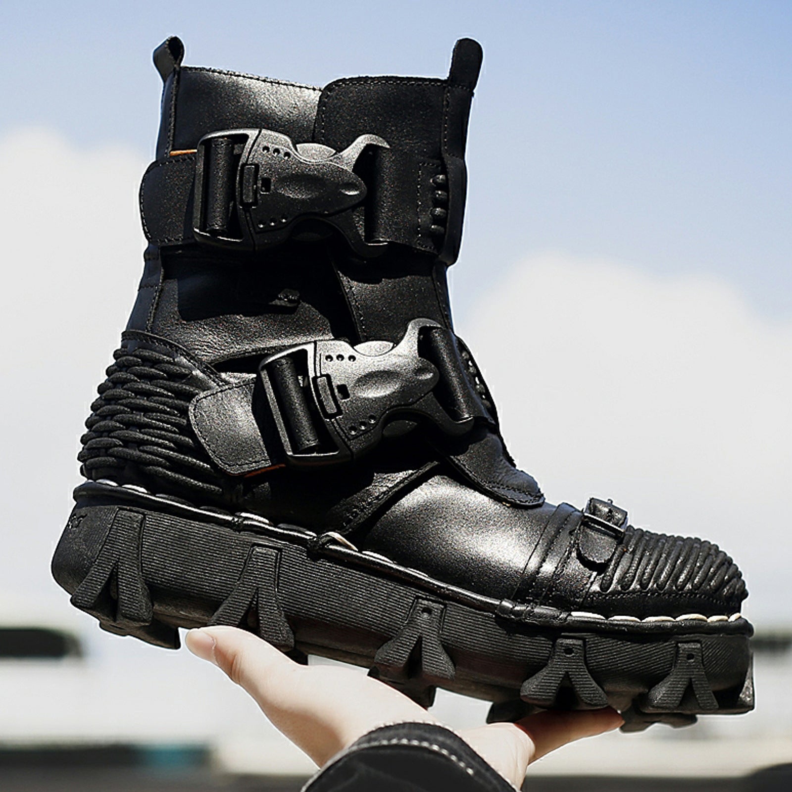 Black high-tech boot with multiple straps held by a hand against a blurred outdoor background