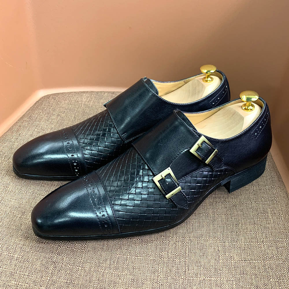 Pair of black leather shoes with gold buckles on a textured surface.
