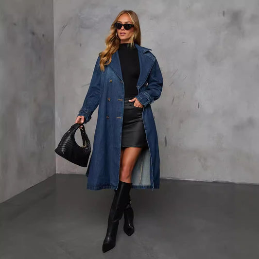 Woman wearing a blue coat, black top, and skirt with black boots against a gray background
