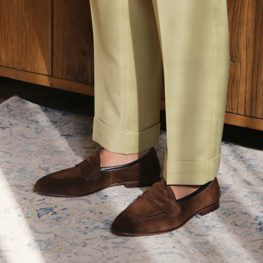 Brown loafers worn with light green pants on a patterned rug.